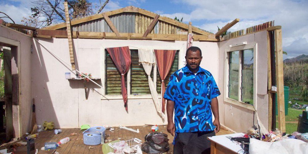 Джон, стоящий рядом с тем, что осталось от его дома после урагана Винстон на Фиджи. (АДРА)