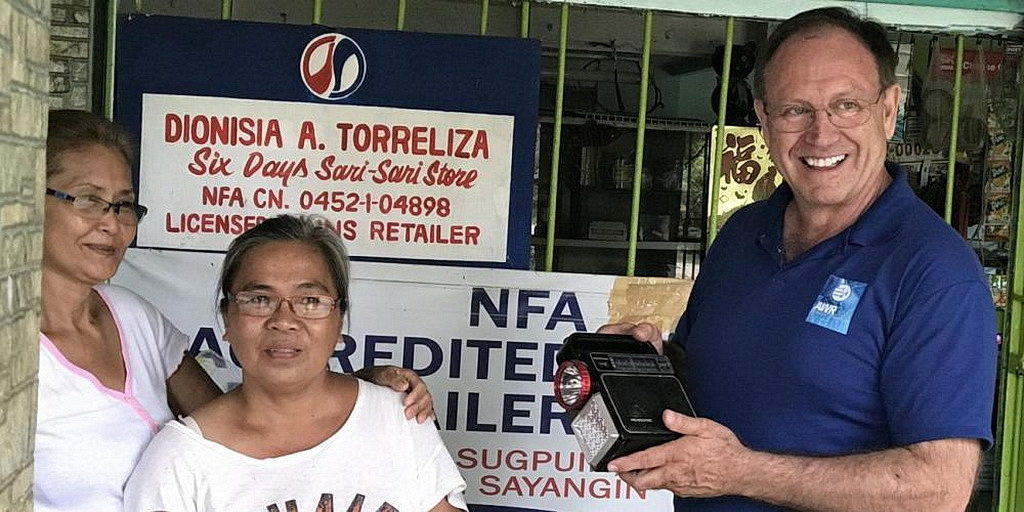 Дуэйн МакКи, справа, держит радиоприемник перед магазином Six Sari-Sari в Калапане, Филиппины. Жители деревни час спускаются с горы, чтобы послушать в магазине Адвентистское Всемирное Радио. [Фото: Адвентистское Всемирное Радио]