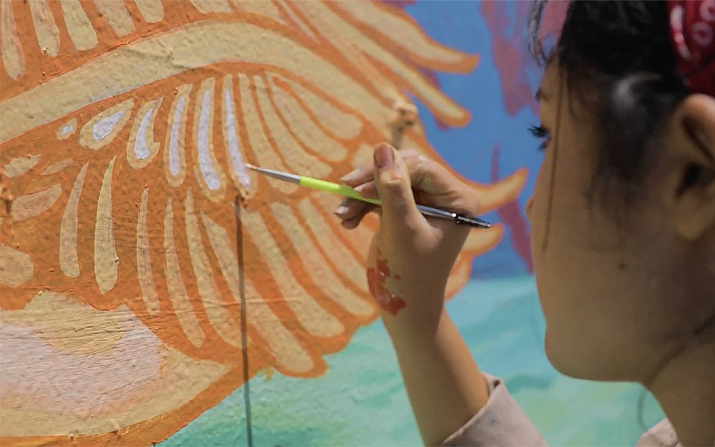 Присцила Ривера, выпускница университета Монтеморелос по специальности "Изобразительное искусство", рисует крылья ангела на фреске "Второе пришествие" в жаркий летний день. [Фото: Adventus]